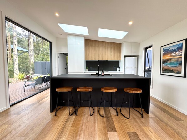 A modern kitchen with a central island, bar stools, skylights, and a view of the outdoors.