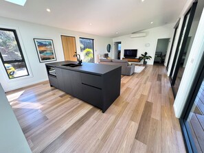 A modern kitchen with a central island, wooden flooring, and large windows.