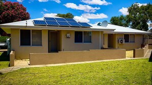 A single-story house with solar panels on the roof, a satellite dish, and a small front yard.