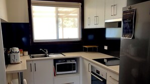 A compact kitchen with white cabinets, a built-in microwave, a black refrigerator, and a window providing natural light.