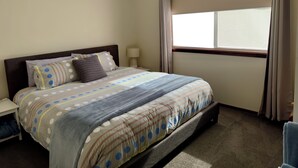A bedroom with a bed, a nightstand, a lamp, an air conditioning unit, and a window with curtains.