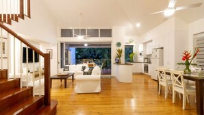 A spacious living area with a wooden staircase, a white sofa, and a dining table with chairs.