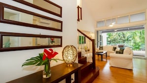 A modern living room with a staircase, a dining area, and a view of greenery outside.