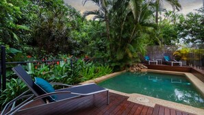 A pool surrounded by lush greenery and a wooden deck with lounge chairs.