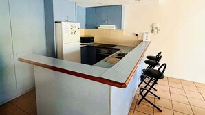 A compact kitchen with a central island, a refrigerator, a stove, and a sink. There are two black bar stools at the island. - Standard Three-Bedroom Villa with Private Pool (Palm Cove)