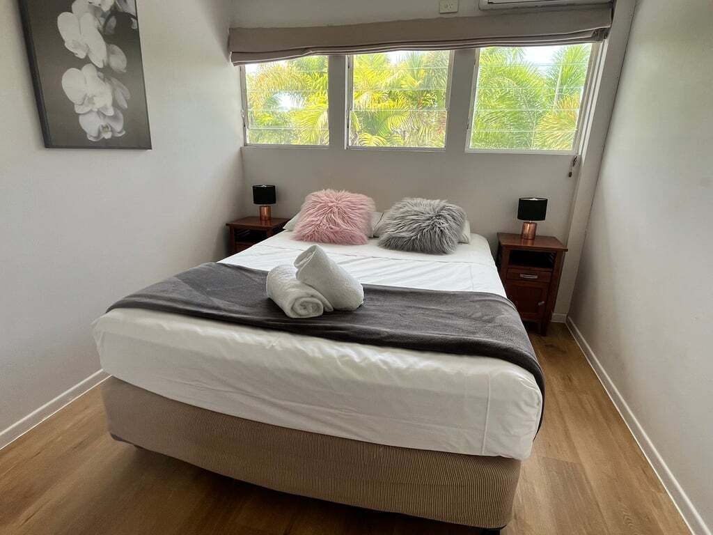 Une chambre à coucher avec un lit, deux tables de chevet, une fenêtre donnant sur un paysage verdoyant et un tableau accroché au mur.
