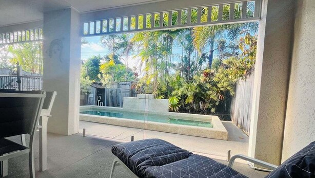 A room with a bed, a small table, and a window overlooking a pool and lush greenery. - Standard Three-Bedroom Villa with Private Pool (Palm Cove)