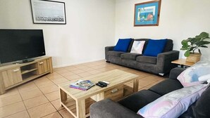 A living room with a flat-screen TV, a grey sofa with blue cushions, a wooden coffee table, and a potted plant. - Standard Three-Bedroom Villa with Private Pool (Palm Cove)