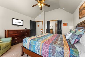 Une chambre à coucher avec un grand lit, une commode en bois, un fauteuil vert et un ventilateur de plafond.