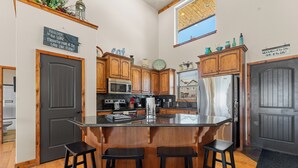 A modern kitchen with wooden cabinets, a central island with stools, a refrigerator, and a microwave. - Pools Pvt Hot Tub near Thunder Ridge & Big Cedar (Hollister)