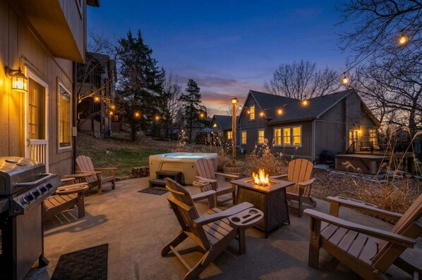 An outdoor patio area with Adirondack chairs, a hot tub, and a fire pit.