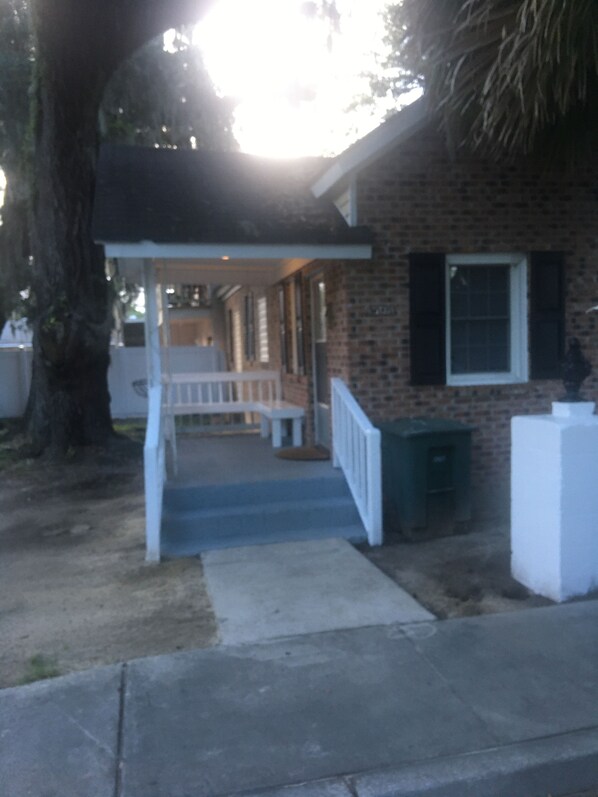 A residential house with a porch, a brick exterior, and a white fence.