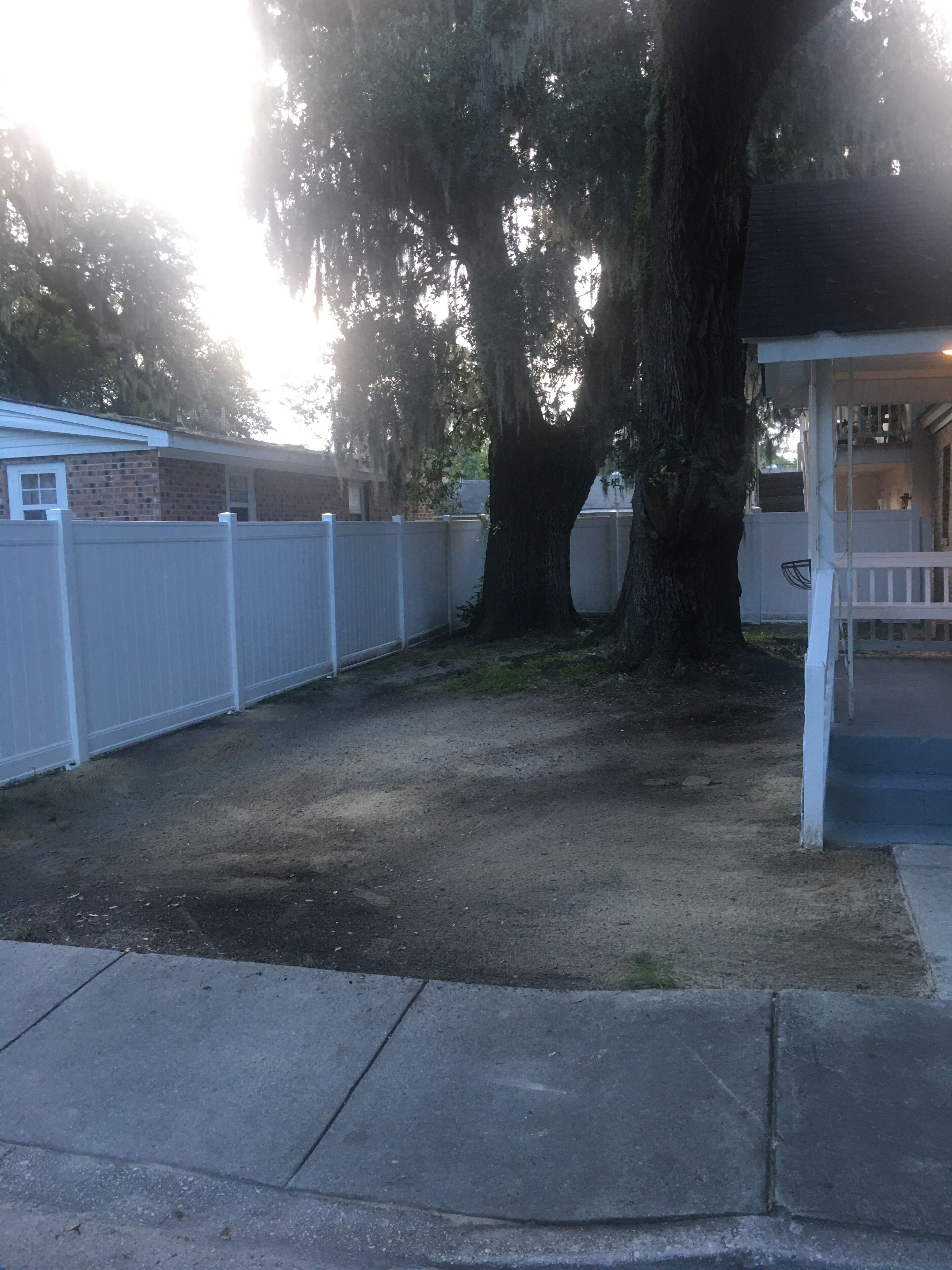 Un patio trasero cercado con un árbol grande, un patio de concreto y una edificación con un porche.