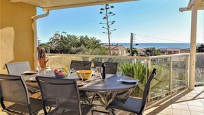 A balcony with a table set for dining, overlooking a coastal view.