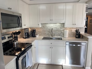 A modern kitchen with white cabinetry, a stainless steel dishwasher, a built-in oven, a coffee maker, and a microwave. - Sunsets and Endless Ocean Views, Beach Front Condo. Seaview Tower 3 #711 (Marco Island)