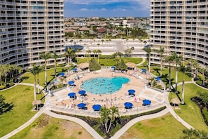 Un hôtel doté d’une piscine centrale, entourée d’espaces de détente et de palmiers.