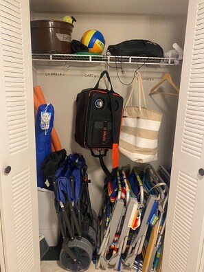 Un placard doté d’étagères, d’une tringle pour suspendre les vêtements, et contenant divers articles, notamment des sacs, des parapluies et un ballon de plage.