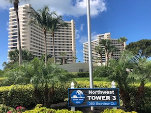A sign for Northwest Tower 3, a high-rise building with multiple balconies, surrounded by lush greenery and palm trees. - Sunsets and Endless Ocean Views, Beach Front Condo. Seaview Tower 3 #711 (Marco Island)