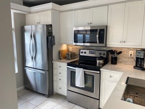 A modern kitchen with stainless steel appliances, including a refrigerator, microwave, and oven. - Sunsets and Endless Ocean Views, Beach Front Condo. Seaview Tower 3 #711 (Marco Island)
