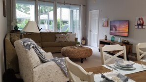 Una sala de estar acogedora con un sofá, una mesa de comedor para dos personas y un televisor en la pared.