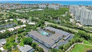 Vista aérea de una zona residencial con un edificio grande que tiene piscina, rodeado de vegetación y una masa de agua.