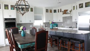 Una cocina moderna con armarios blancos, una isla central con taburetes de bar, horno empotrado y refrigerador de acero inoxidable.