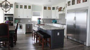 Una cocina moderna con armarios blancos, una isla grande con taburetes de bar, un refrigerador de acero inoxidable y una araña.