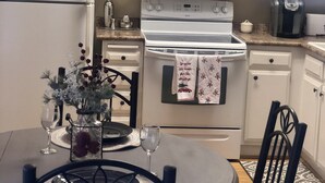 Une cuisine avec des meubles blancs, un micro-ondes noir, une cuisinière blanche et une table à manger avec des chaises.