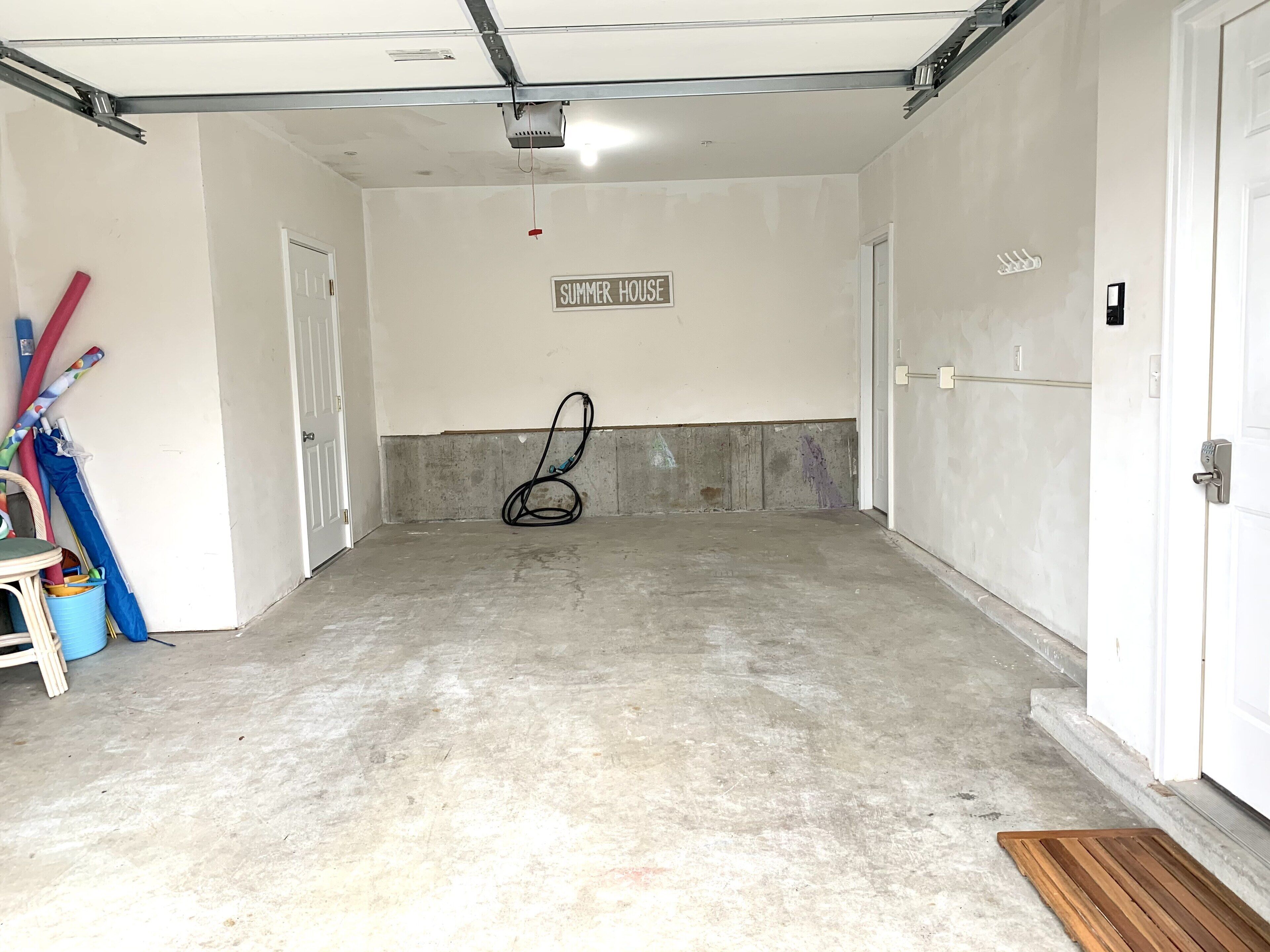 A clean, empty garage with a concrete floor, a ceiling fan, and a sign reading "SUMMER HOUSE".