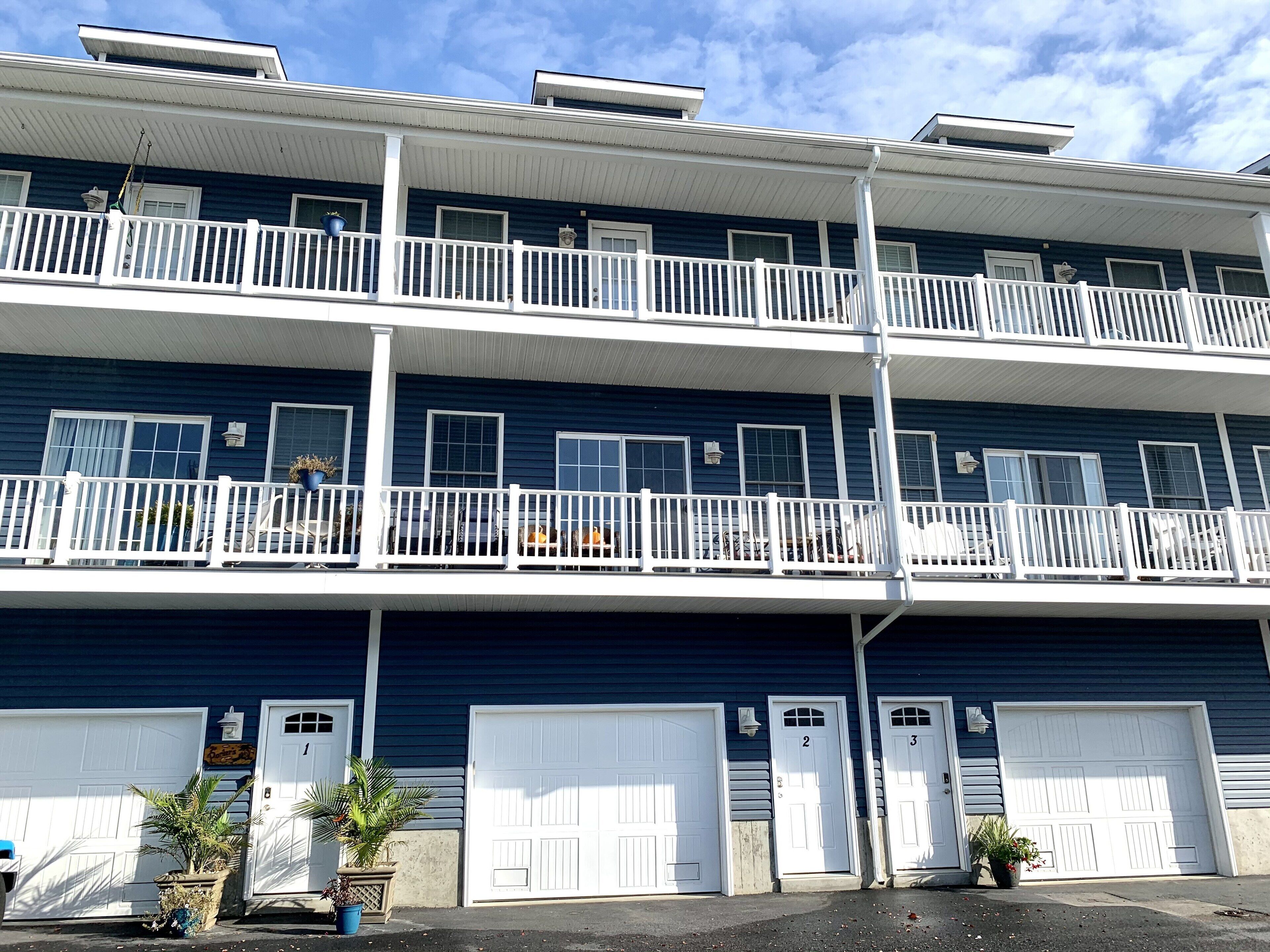 A multi-story residential building with white railings, multiple garage doors, and potted plants.