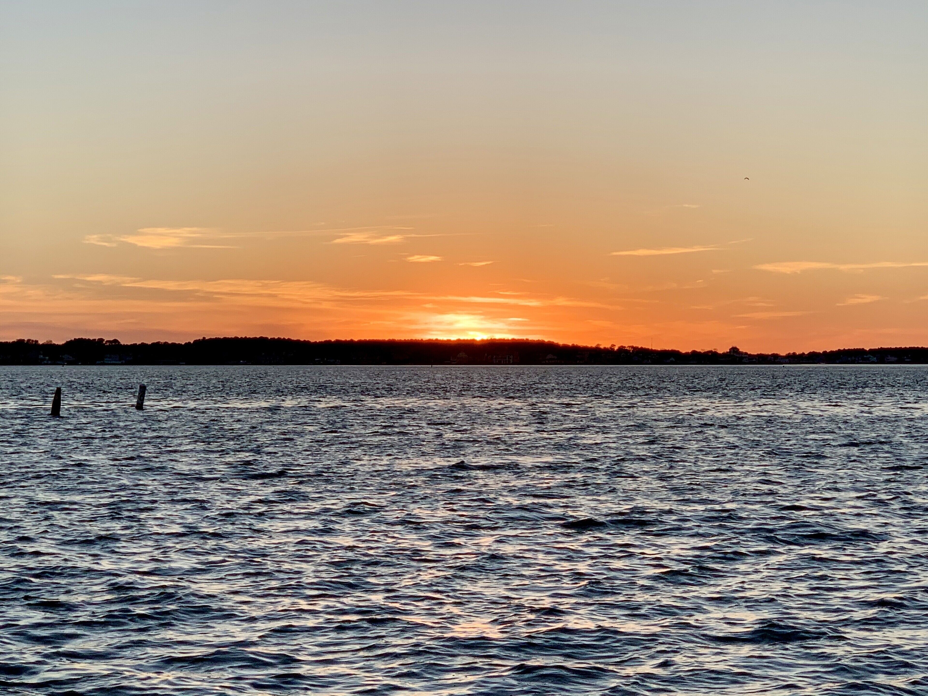 Ein Sonnenuntergang über ruhigem Wasser, im Hintergrund eine Küste.