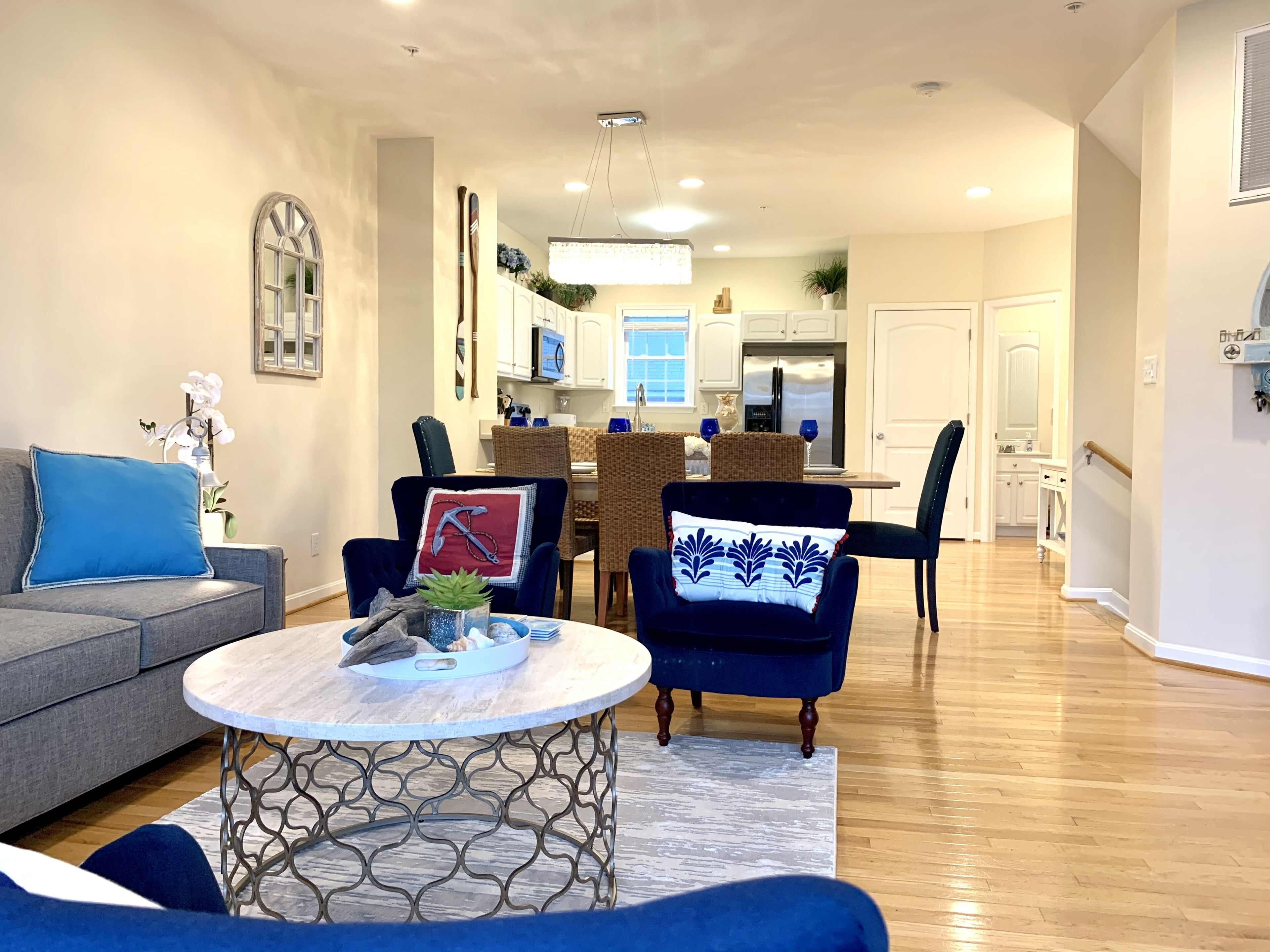 A modern living room with a grey sofa, blue armchairs, a round coffee table, and a dining area with a wooden table and chairs.