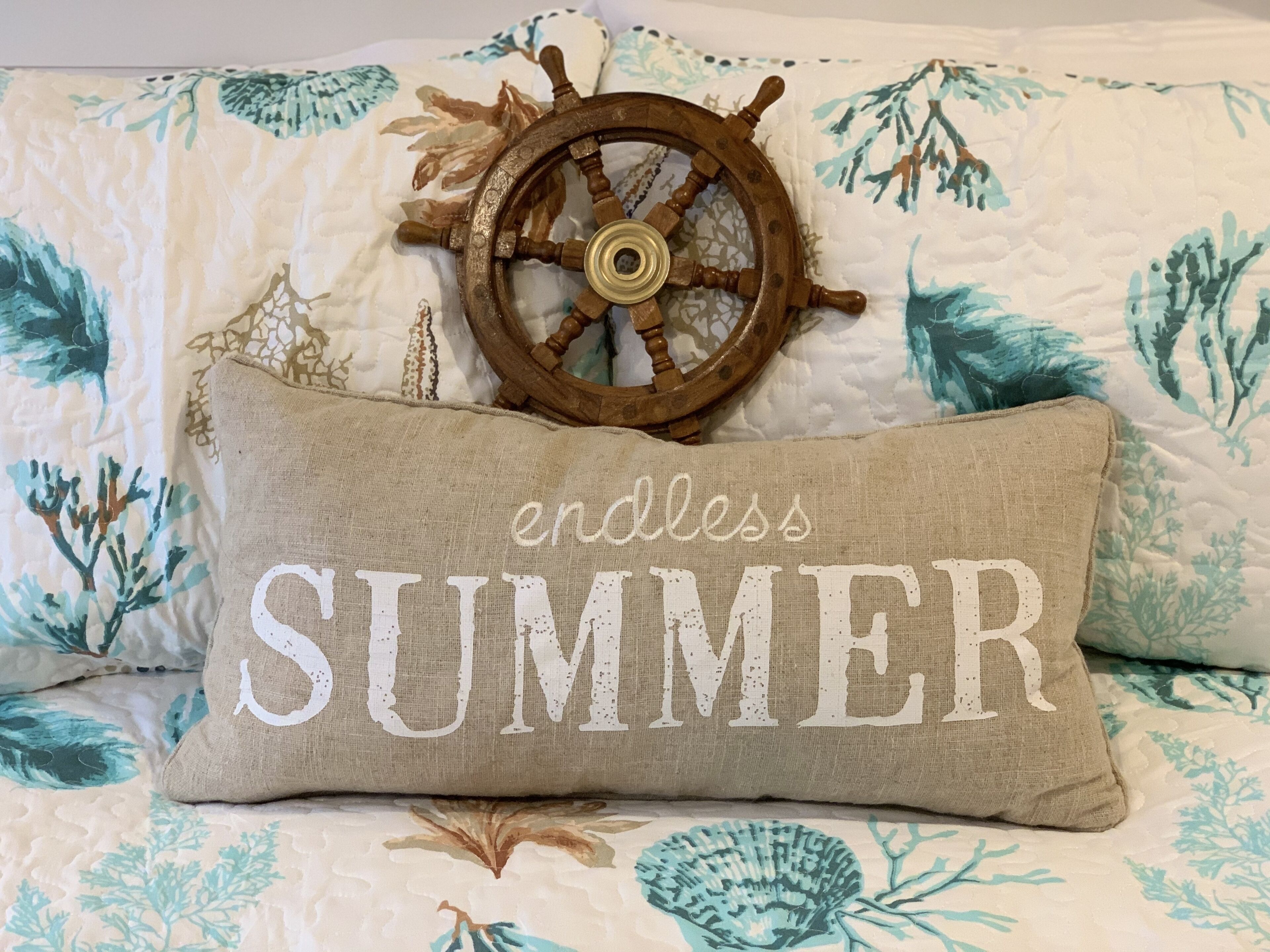 En seng med et blomstret sengetæppe, et dekorativt træhjul og en pude med teksten "endless SUMMER".