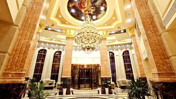A grand lobby with a large chandelier, marble columns, and a central circular ceiling artwork. - City Vogue Hotel (Nantong)