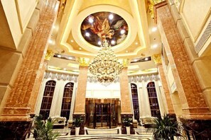 Een statige lobby met een grote kroonluchter, marmeren zuilen en een rond centraal plafondkunstwerk.