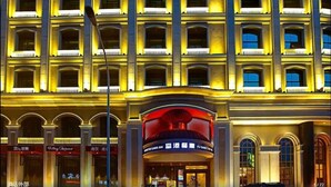 A multi-story hotel with a classical architectural style, featuring a prominent entrance with a red-lit marquee. - City Vogue Hotel (Nantong)
