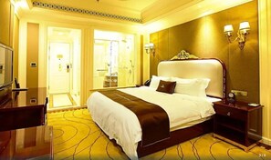 A hotel room with a large bed, a desk, and a bathroom visible through an open door. - City Vogue Hotel (Nantong)