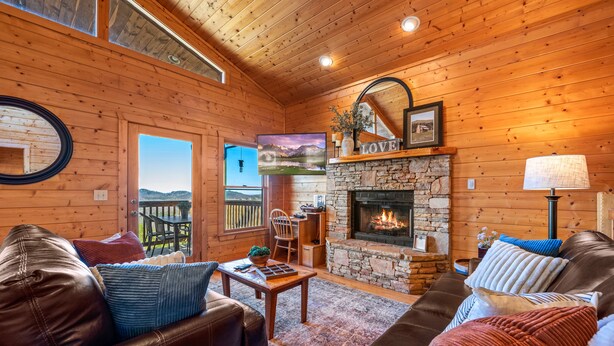 Interior acogedor de una cabaña de madera con chimenea de piedra, muebles de cuero y una vista panorámica a través de la puerta.