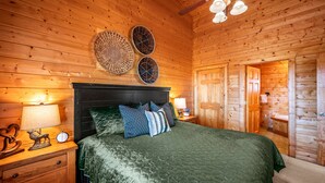 Dormitorio con paneles de madera, una cama, mesitas de noche y un ventilador de techo.
