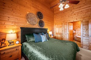 Ein Schlafzimmer mit Holzwänden, einem Bett, Nachttischen und einem Deckenventilator.