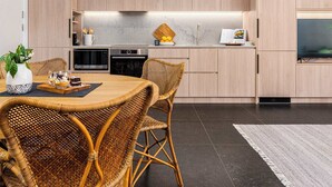 A modern kitchen with built-in appliances, a dining area with wicker chairs, and a large TV. - The Arden 1 Coogee New large Beachside Garden Apt (Sydney)