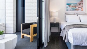 A modern hotel room with a bed, bedside table, lamp, and a painting of a coastal scene. - The Arden 1 Coogee New large Beachside Garden Apt (Sydney)