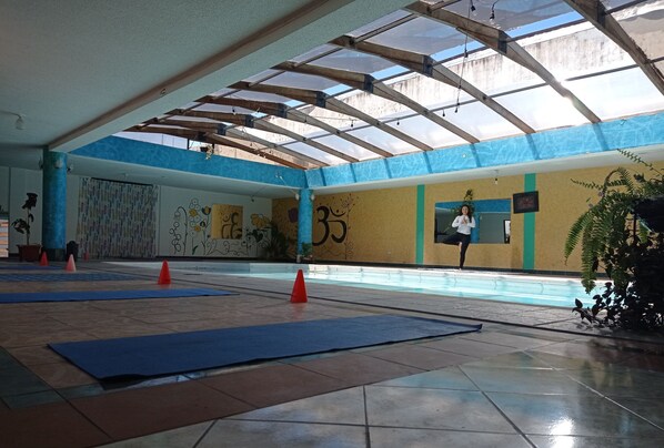Experience a serene space with a high ceiling, glass roof, and vibrant murals, perfect for yoga or relaxation.