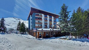 Un hotel de varios pisos con un telesilla al fondo, rodeado de nieve y árboles.