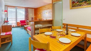 Comedor con mesa de madera para cuatro personas, lámpara colgante roja y un cuadro en la pared.