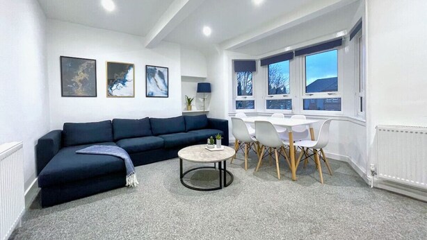 Una sala de estar moderna con un sofá azul oscuro, una mesa de centro redonda y un comedor con sillas blancas y una mesa.
