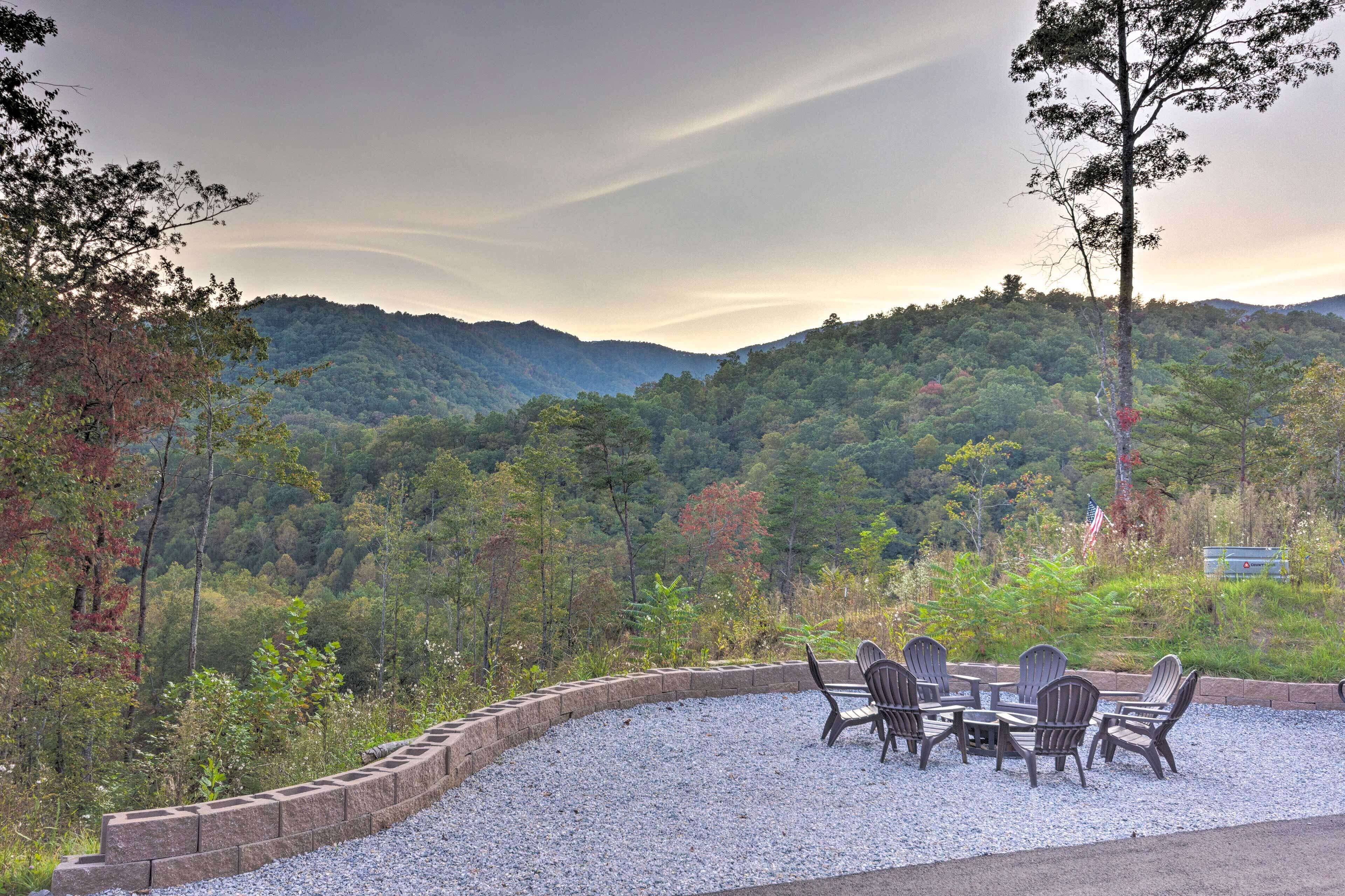 A patio with Adirondack chairs and a table, surrounded by a stone wall, overlooking a forested mountain range.