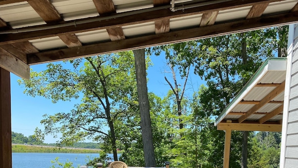 Una terraza de madera con un trampolín, una mesa y sillas, con vista a un lago.