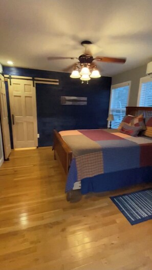 Un dormitorio con cama, piso de madera, ventilador de techo y ventana.