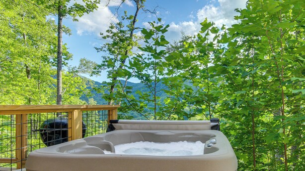 Un jacuzzi en una terraza con vistas a un bosque y montañas.